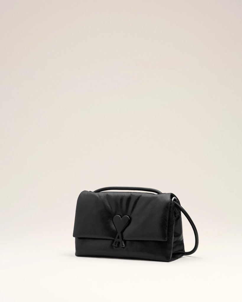 Black leather handbag with a heart-shaped clasp on a pale beige background.