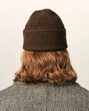 Back view of a person wearing a dark brown knit beanie and a black-and-white herringbone coat, blonde hair peeking from below the hat