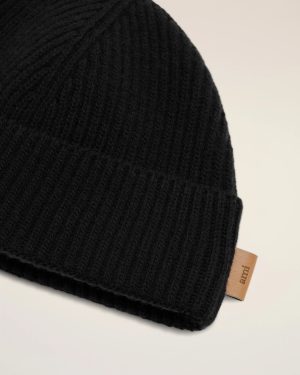 Close-up of a black knit beanie with a tan leather logo tag at the bottom edge.