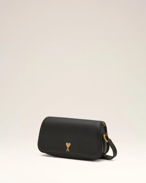 Black leather crossbody bag with a small gold heart clasp on a light beige background.