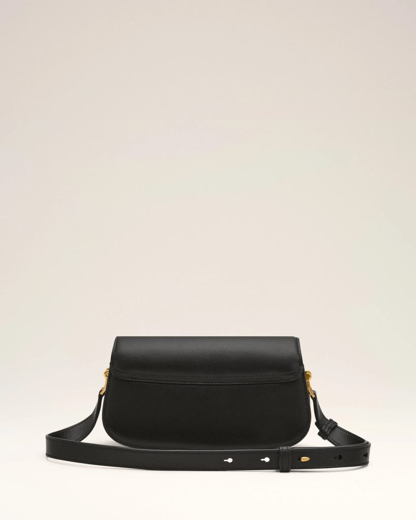 Black leather crossbody bag with a long strap and gold hardware against a light background.