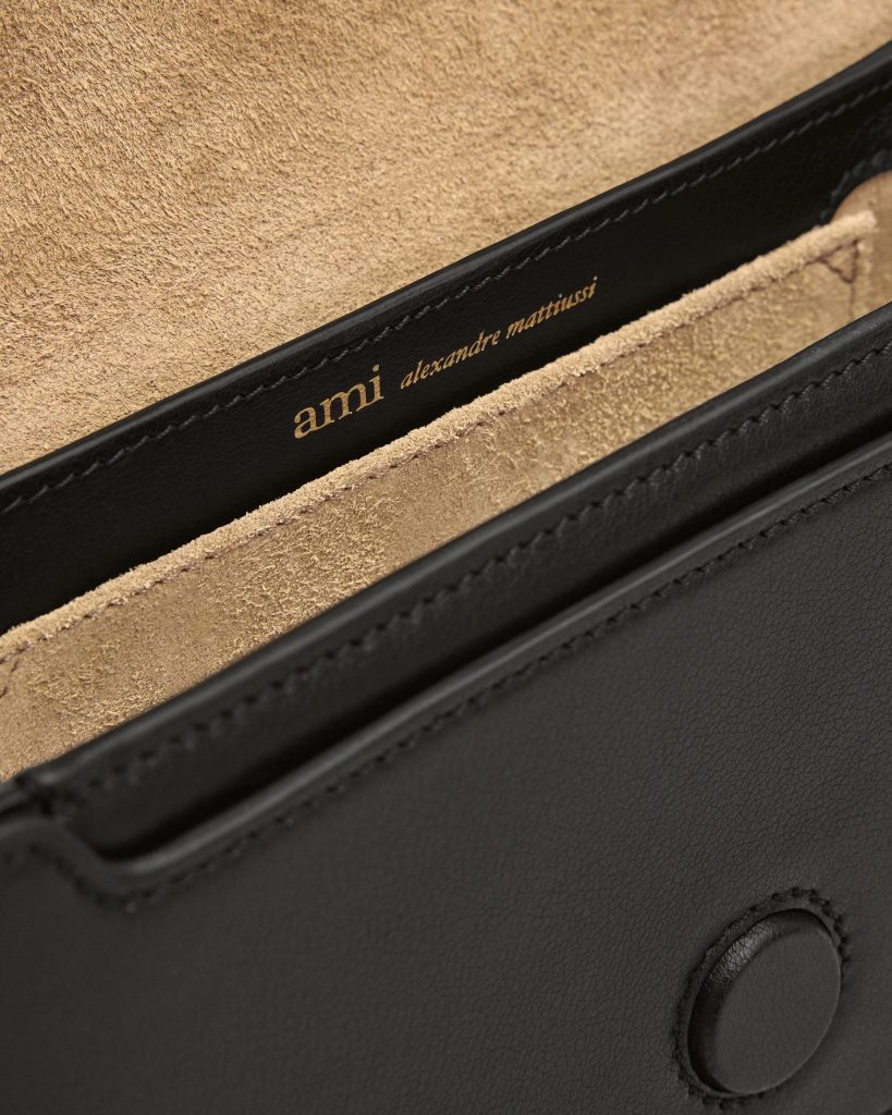Gold embossed text reading 'ami alexandre mattussi' along the black leather trim of a bag, with beige suede interior visible.
