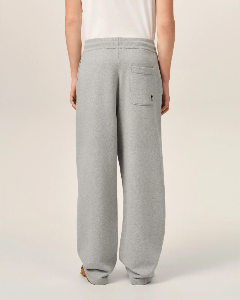 Back view of a person wearing light gray sweatpants with a patch pocket and a small black heart logo on the pocket.