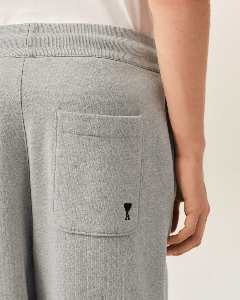 Close-up of gray sweatpants pocket with a small black heart-and-ribbon logo near the seam on a person’s hip.