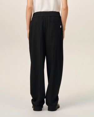 Back view of a person wearing black wide-leg pants with an elastic waistband and a white top, showing a rear pocket and relaxed fit against a light background.