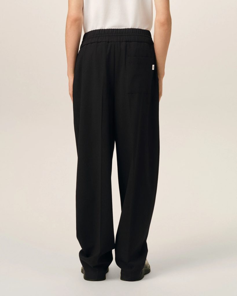 Back view of a person wearing black wide-leg pants with an elastic waistband and a white top, showing a rear pocket and relaxed fit against a light background.
