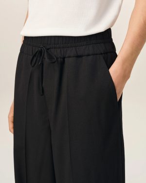 Close-up of a person wearing a white textured knit top and black, elastic-waist pants with a drawstring and side pocket visible.
