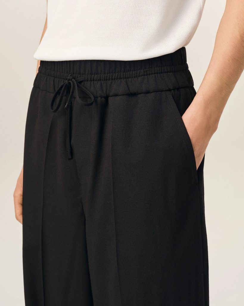 Close-up of a person wearing a white textured knit top and black, elastic-waist pants with a drawstring and side pocket visible.