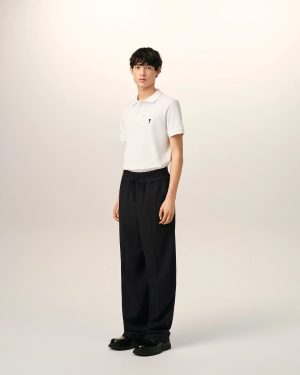 Full-body portrait of a person wearing a white polo shirt, black drawstring pants, and black shoes, standing against a light backdrop