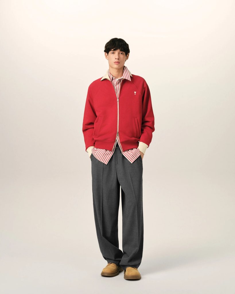 Young man in a red zip-up jacket over a red-and-white striped shirt, standing against a light background.