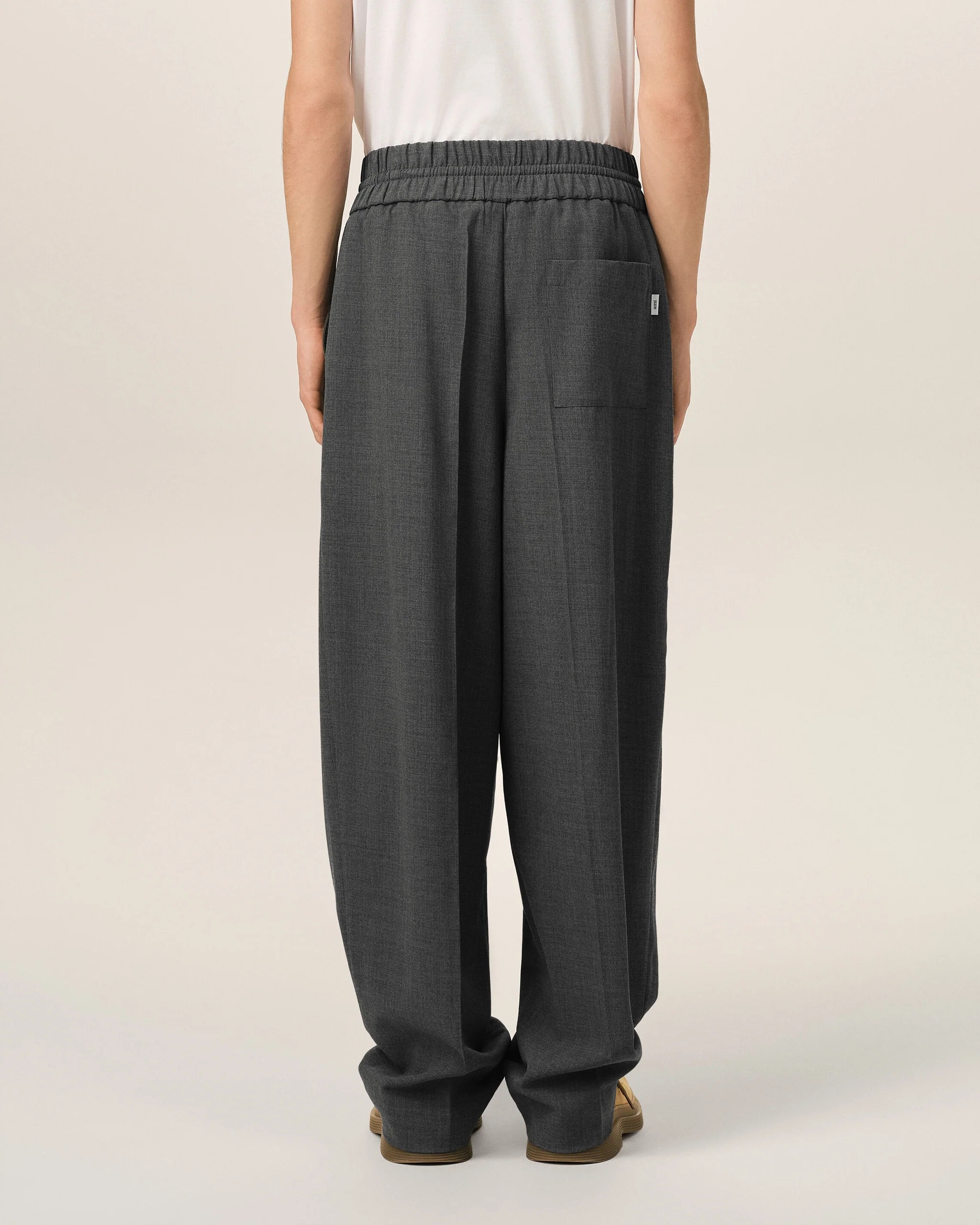 Image 141 - New Trend Back view of a person wearing dark gray, wide-leg pants with an elastic waistband and a rear pocket, paired with a white top and tan shoes.