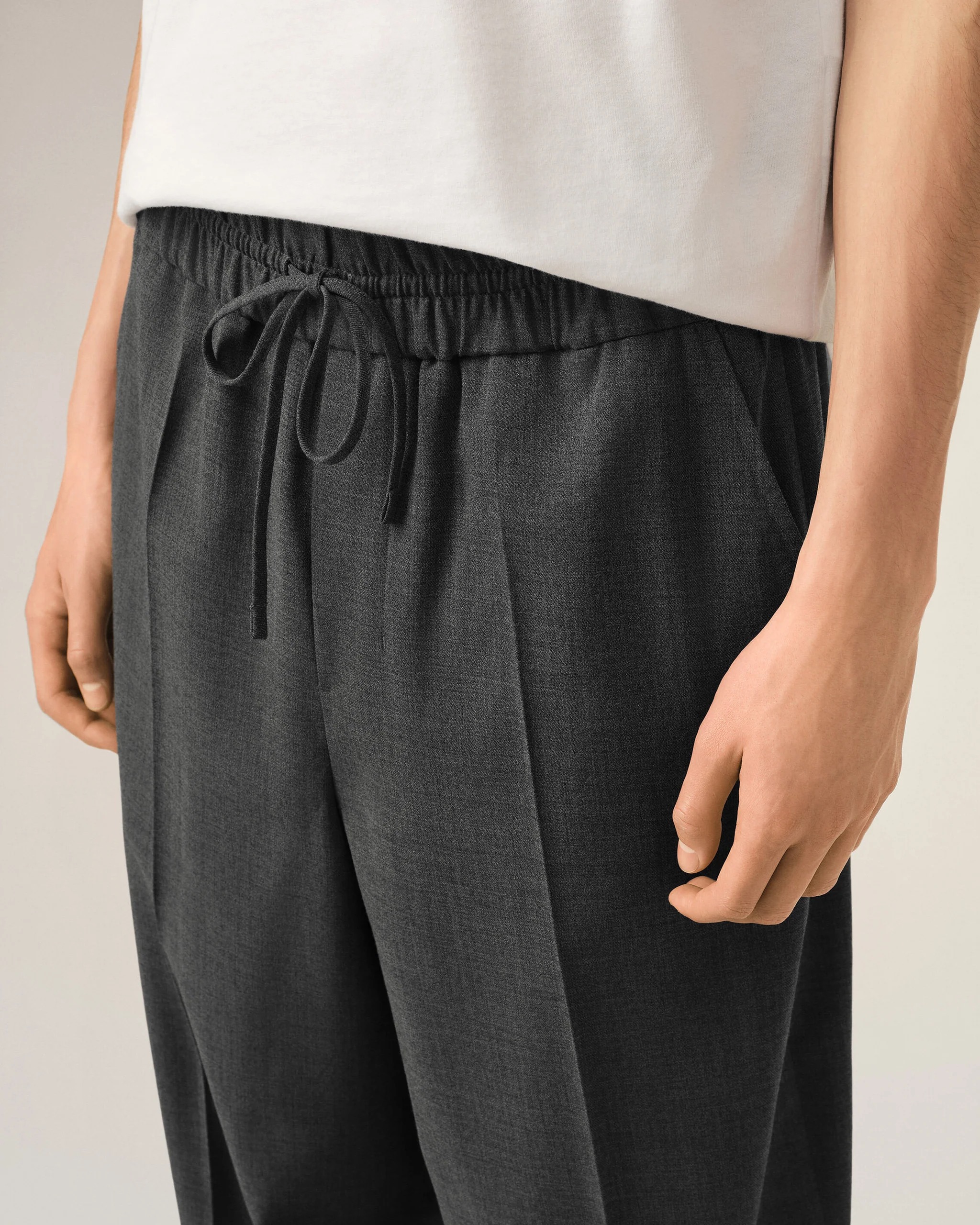 Image 142 - New Trend Close-up of a person wearing a white top tucked into dark gray drawstring trousers at the waist.