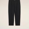Pair of black tailored trousers with front pleats and cuffed hems, photographed against a light beige background