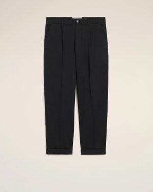 Pair of black tailored trousers with front pleats and cuffed hems, photographed against a light beige background