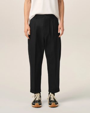 Lower half of a person wearing black cuffed trousers with a white top and black-and-white sneakers with tan soles.