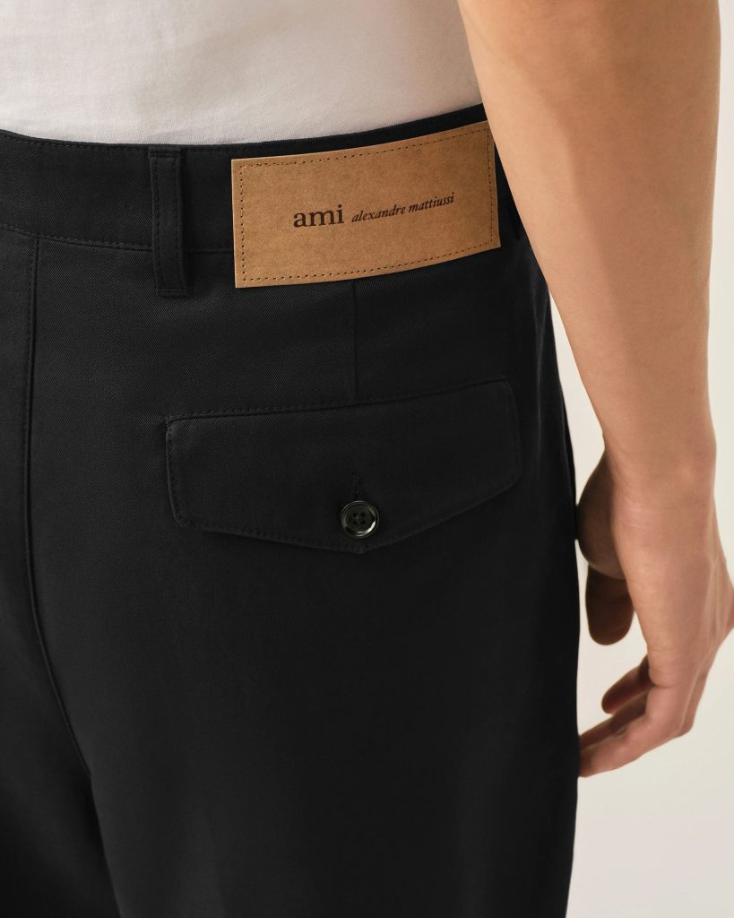 Tan leather brand patch on the back waistband of black trousers, reading 'ami alexandre mattiussi'.