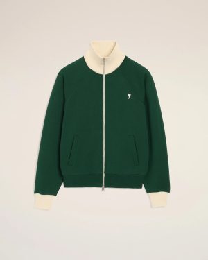 Green zip-up jacket with cream ribbed collar and cuffs, small white heart emblem on the left chest.