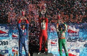 Podium celebration with three race winners holding trophies as confetti rains down.
