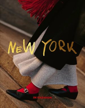 Gold 'New York' text overlaying a person in a black coat, gray skirt, red socks, and black loafers on stone steps.