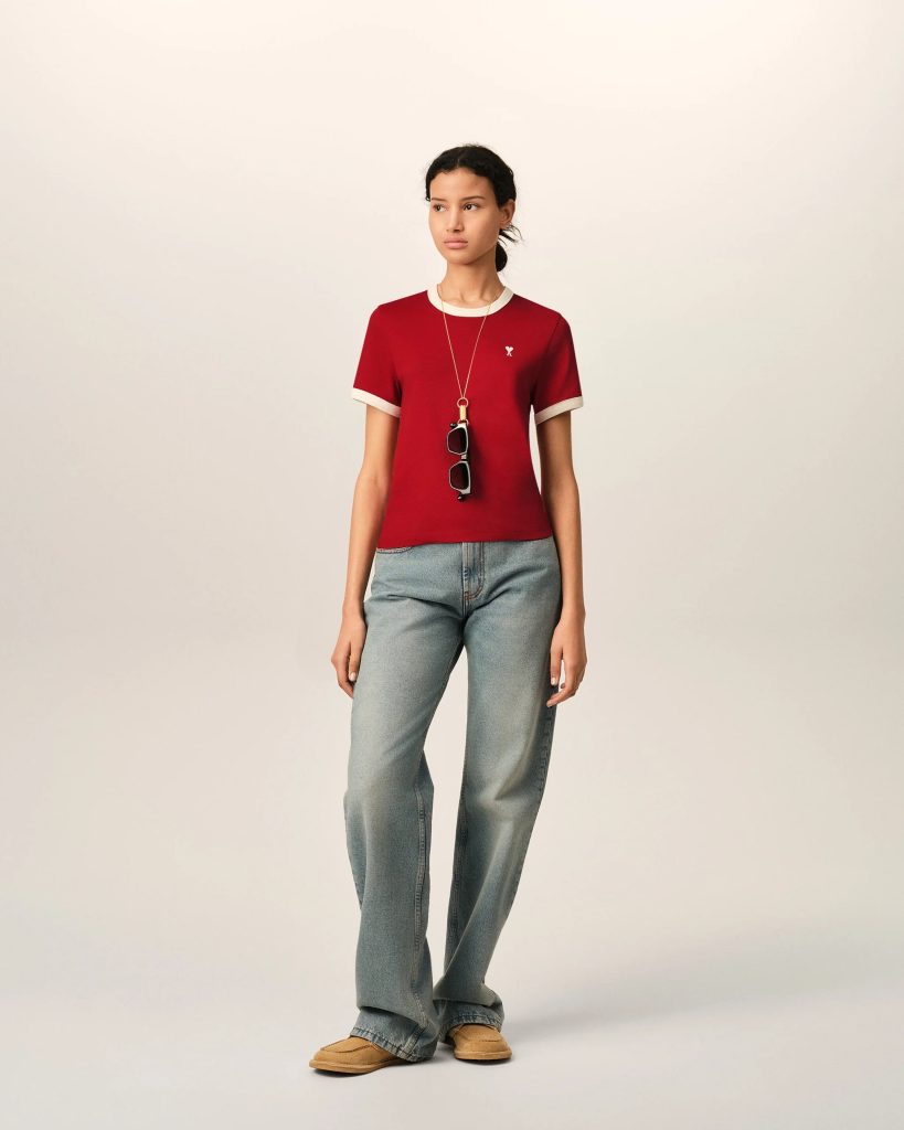 Young woman modeling casual red short-sleeve top with white collar and cuffs, jeans, and tan shoes, wearing sunglasses hanging from a necklace.