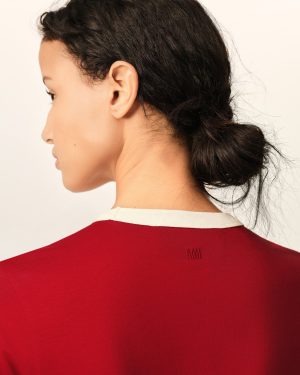 Side profile of a woman with dark hair pulled back in a low bun, wearing a red shirt.