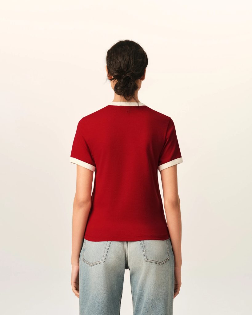Back view of a person wearing a red short-sleeve shirt with white cuffs and light-blue jeans, standing against a pale background.