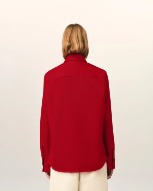 Person seen from behind wearing a red jacket, blonde hair, and light-colored pants against a pale background