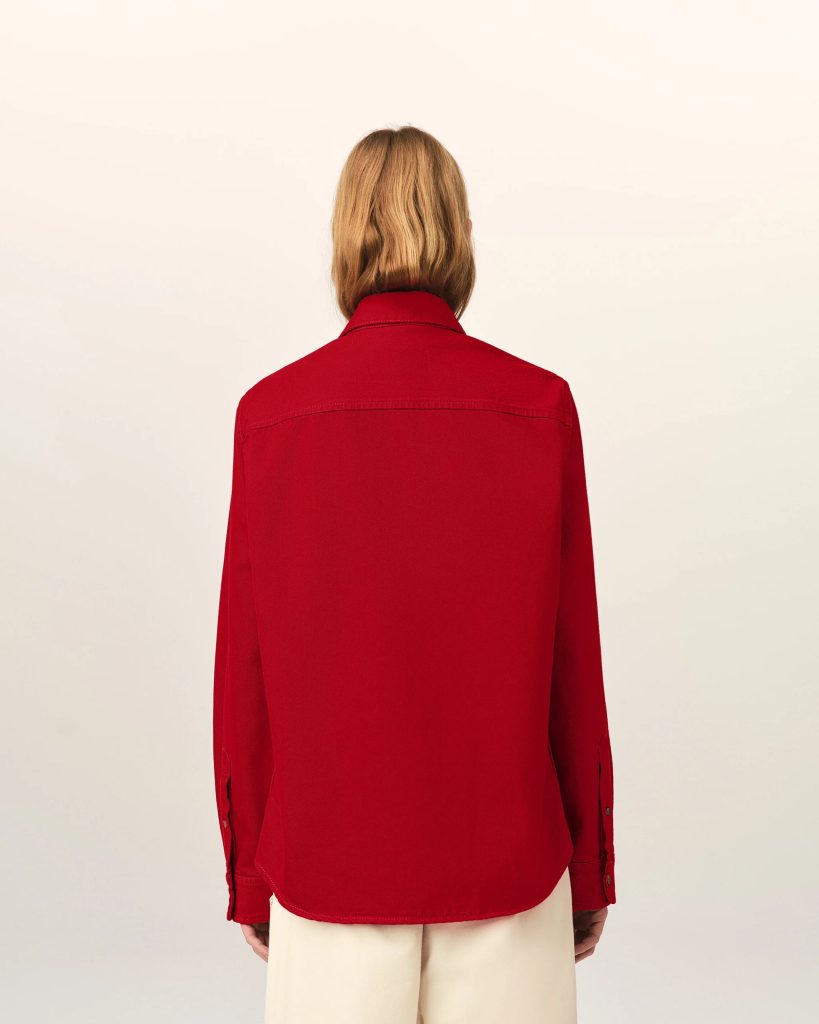 Person seen from behind wearing a red jacket, blonde hair, and light-colored pants against a pale background