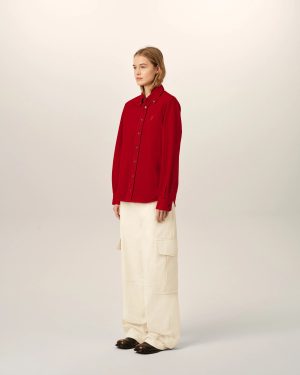Person model wearing a red button-down shirt and beige cargo pants, standing against a plain light backdrop, facing left in a mid-profile pose.