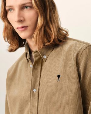 Close-up of a person wearing a beige corduroy shirt with a small black heart and A embroidery on the chest.