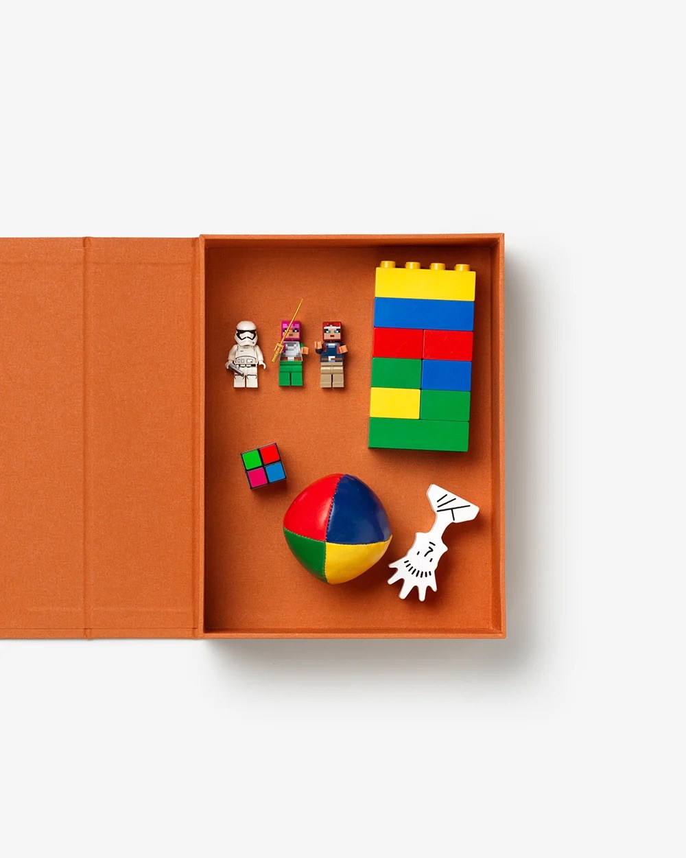 Image 189 - New Trend Open orange box with colorful building bricks, a multicolored ball, small figurines, a tiny cube, and a white hand-shaped toy.