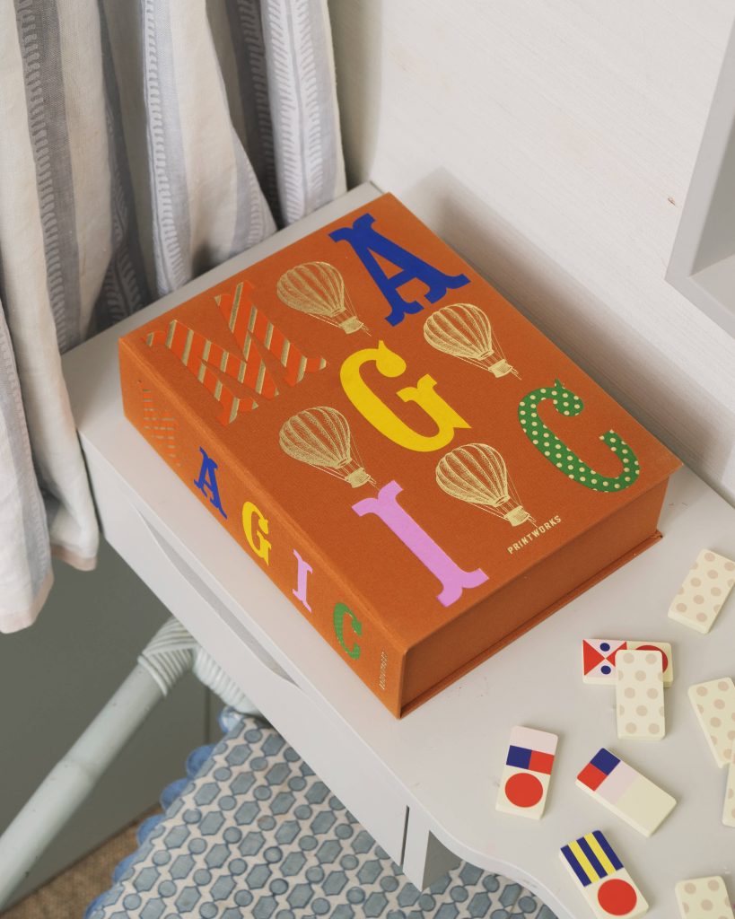 Orange children's book with colorful letters and balloon illustrations on a white shelf beside a striped curtain.