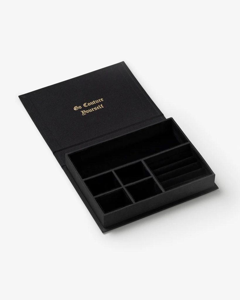 Open black jewelry organizer with multiple compartments; gold text on the lid reads 'Go Couture Yourself'.