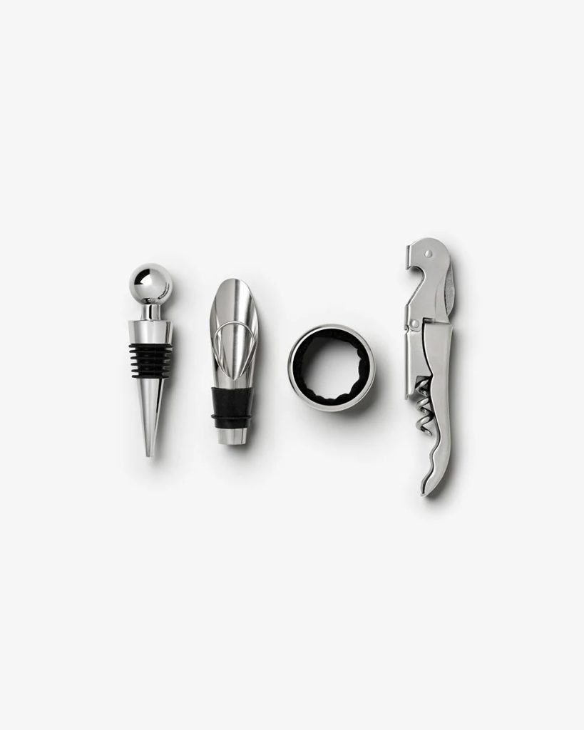 Set of stainless steel wine accessories: stopper, pourer, foil cutter, and corkscrew arranged in a row