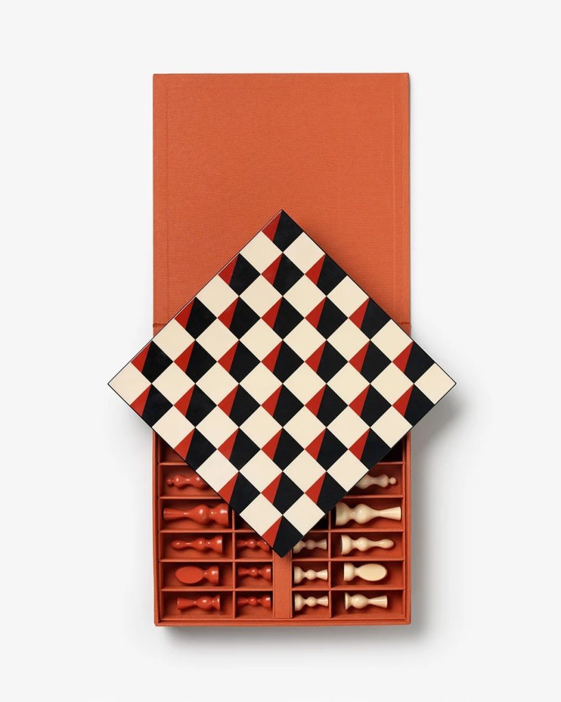 Open orange box revealing a diamond-shaped checkered board resting on top of a tray filled with red and cream game pieces.