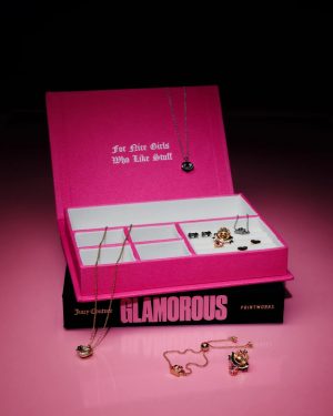 Open pink jewelry box with a necklace hanging from the lid and multiple rings and pendants arranged in compartments;‘For Nice Girls Who Like Stuff’ visible on the lid, with a black Glamorous box underneath.
