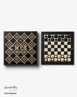 Luxurious black and gold chess set with a geometric diamond-pattern box; board beside shows starting positions of black and white pieces.