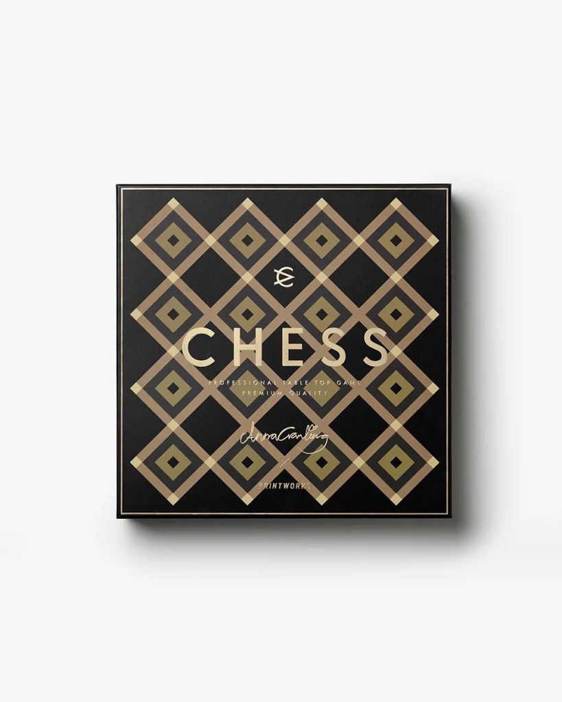 Black square box with a gold diamond lattice pattern, featuring the large word CHESS and a signature at the bottom.