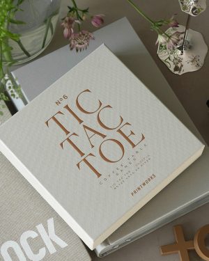 White textured book titled 'No.6 Coffee Table' in copper letters on a table with flowers and a decorative lamp nearby.
