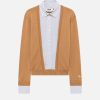 Camel-colored cardigan over a light blue striped button-down shirt with cuffs showing.
