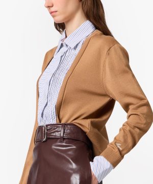 Side view of a woman in a camel cardigan over a blue striped button-down shirt, tucked into a dark burgundy leather skirt with a belt.