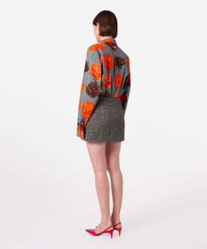 Back view of a woman wearing a gray rose-print blouse with orange roses, a metallic mini skirt, and pink heeled sandals/pumps.