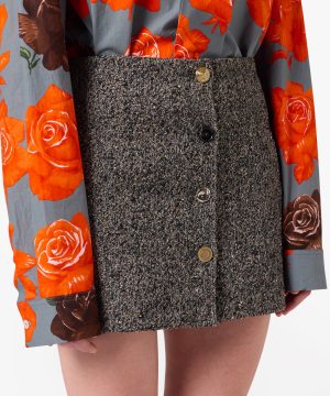 Close-up of a textured gray tweed mini skirt with button closures, paired with a gray blouse featuring large bright orange roses.