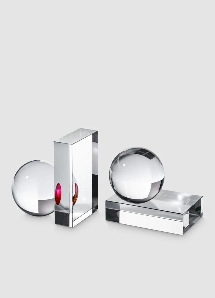 Decorative crystal spheres and rectangular prisms arranged on a light gray background, reflecting light like glass sculptures