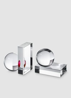 Three transparent glass objects: a sphere on the left, a tall rectangular prism with a pink accent, and a sphere resting on a rectangular base to the right, all on a light gray background.