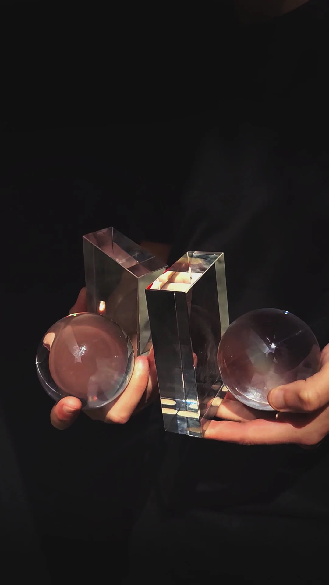 Image 267 - New Trend Two clear glass spheres held in hands with a tall, angular crystal trophy between them against a dark background, likely an awards presentation set.