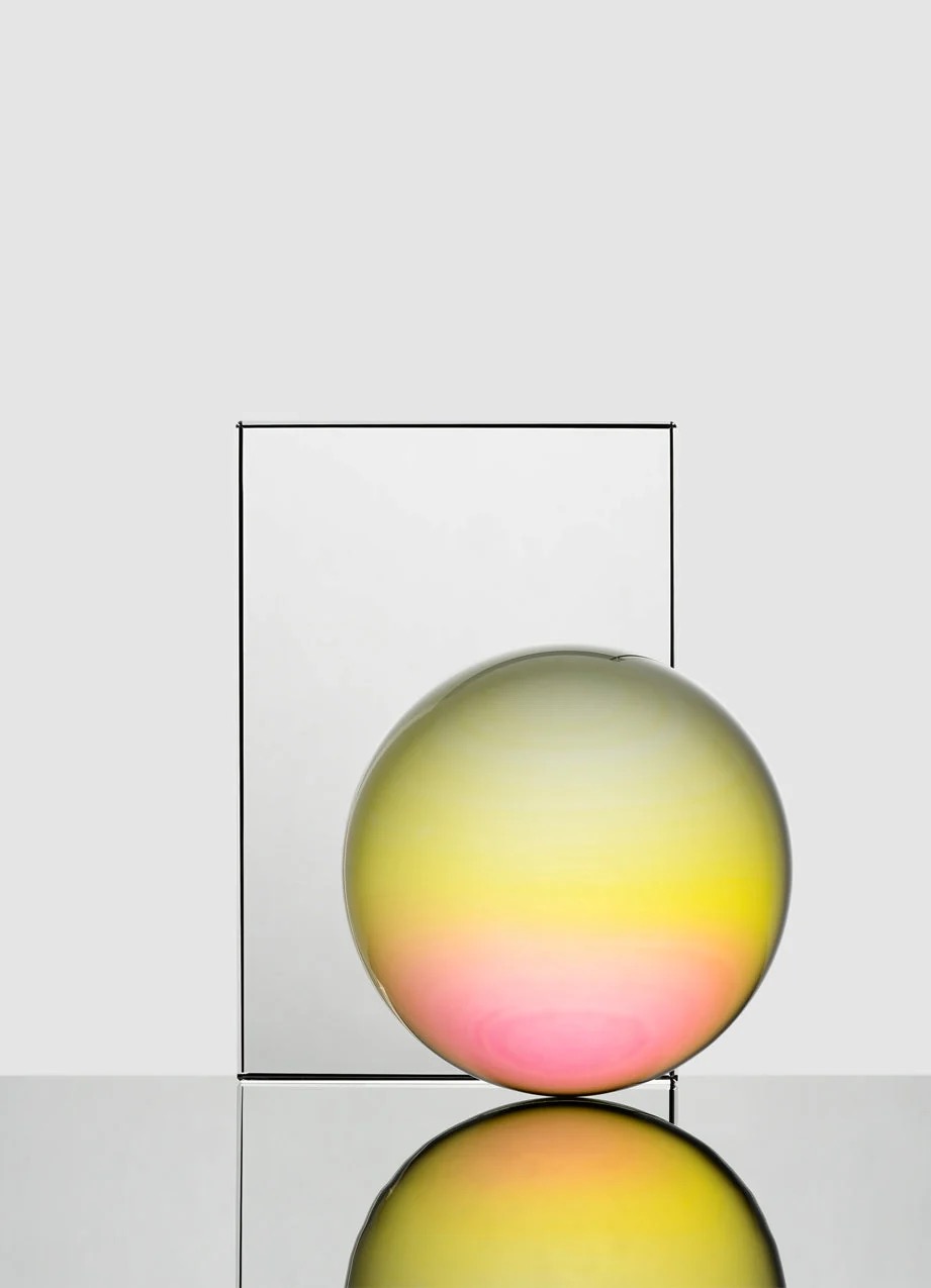 Image 268 - New Trend Glossy glass sphere with a yellow-to-pink gradient sits beside a tall rectangular frame, reflected on a glossy surface.