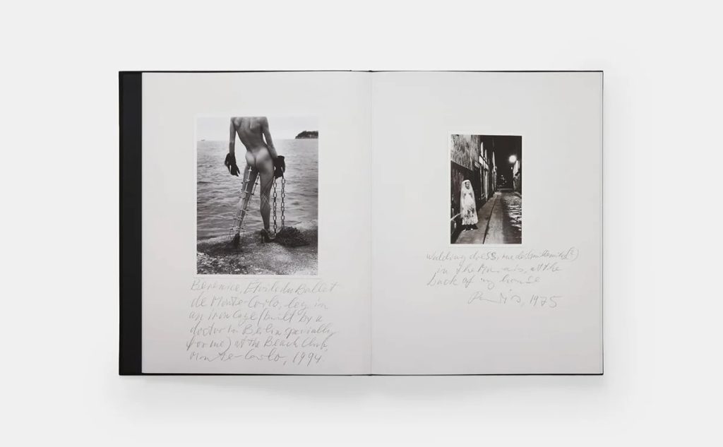 Open book showing two black-and-white photographs with handwritten captions on white pages; left image depicts a nude figure by the water with chains, right image shows a street scene with a figure in a coat.