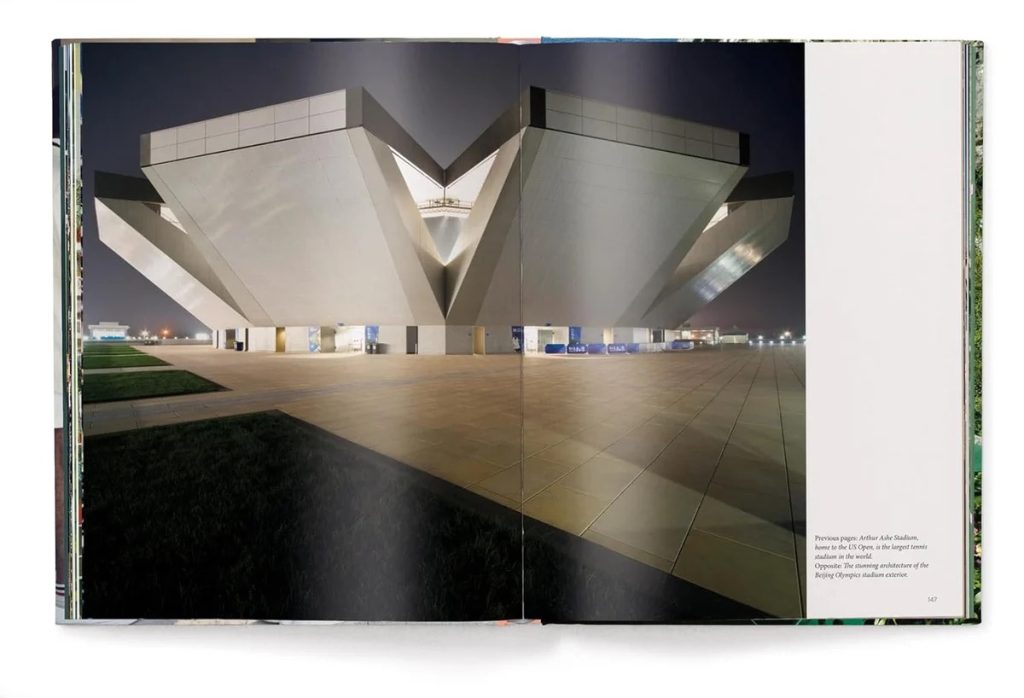 Night view of a futuristic, angular white stadium with sloped concrete wings and a reflective tiled plaza in front.