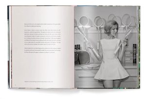 Open magazine spread: left page with paragraphs of text; right page shows a vintage black-and-white photo of a woman in a short dress holding two tennis rackets in a retro kitchen setting.